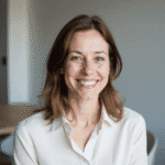 Realistic portrait of a 34-year-old woman, simple and natural appearance, everyday French woman, friendly smile, medium-length chestnut brown hair, casual yet professional style. Wearing modest, elegant clothing (like a light blouse or simple shirt), with very light natural makeup. She should look approachable, authentic, and relatable — not like a model but like an ordinary woman who found success in her career. Bright, neutral background, modern photo style, professional portrait framing.